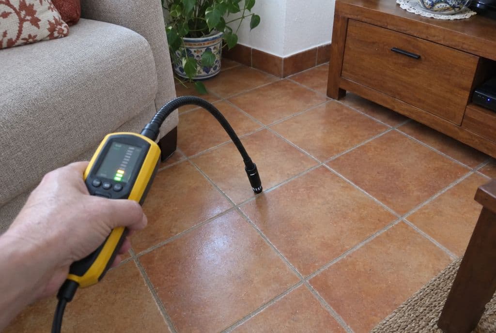 Mano con un detector de hidrógeno de sonda flexible rastreando las juntas del suelo de un salón