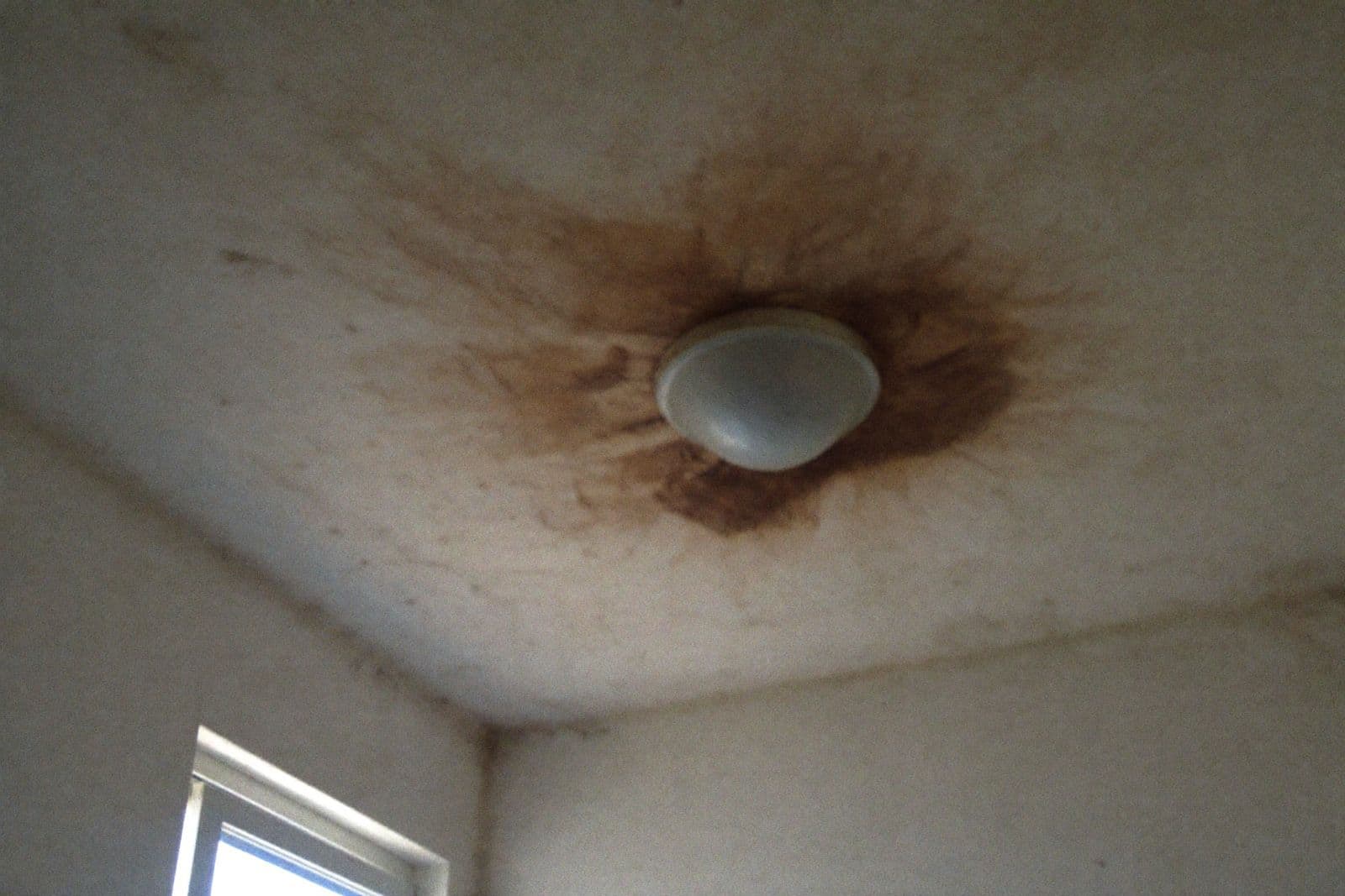 Mancha de humedad marrón alrededor de la lámpara del techo de un baño