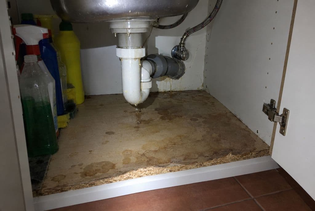 Mueble bajo el fregadero con la base hinchada y manchada por una fuga
