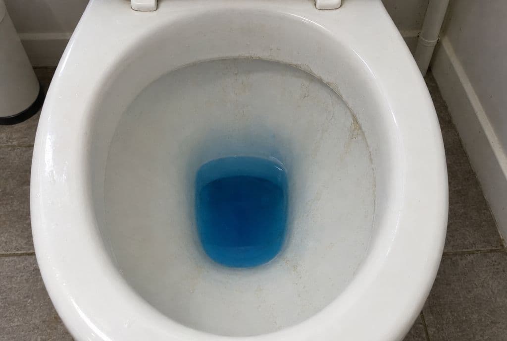 Agua azul en el fondo de la taza del inodoro tras echar colorante en la cisterna