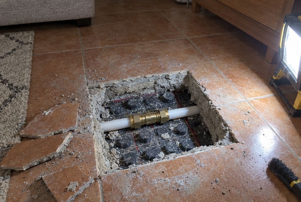 Cata cuadrada en el suelo de baldosa con el tubo del suelo radiante reparado con un manguito de latón