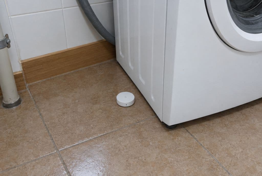 Sensor de fuga de agua redondo en el suelo junto a una lavadora