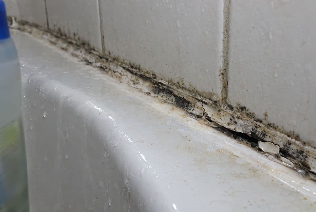 Junta de silicona ennegrecida y despegada entre la bañera y el alicatado