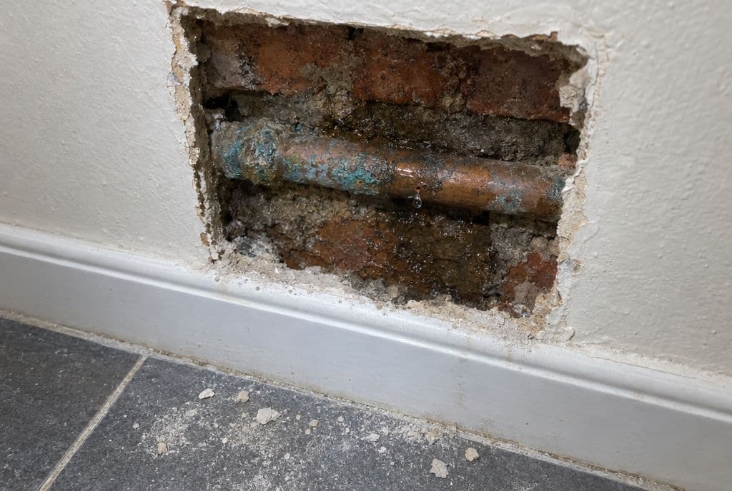 Cata en el enlucido de un baño con una tubería de cobre corroída y el ladrillo húmedo alrededor