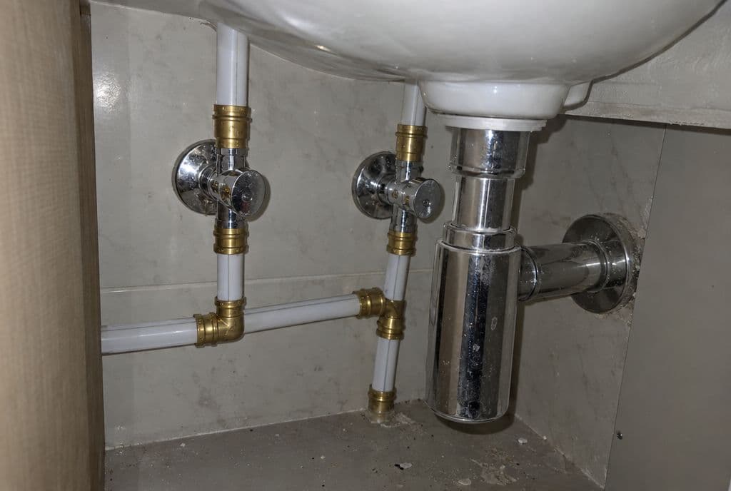 Tuberías multicapa blancas con racores de latón bajo un lavabo