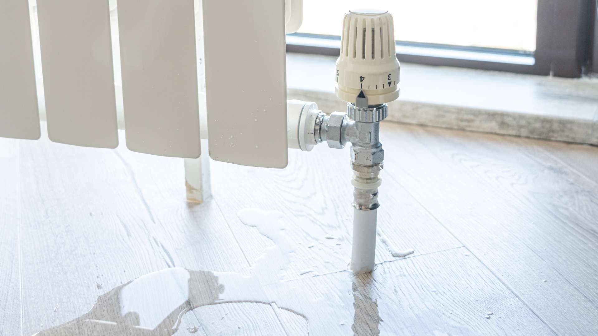 Fuga de agua en la llave de un radiador de calefacción sobre suelo de madera
