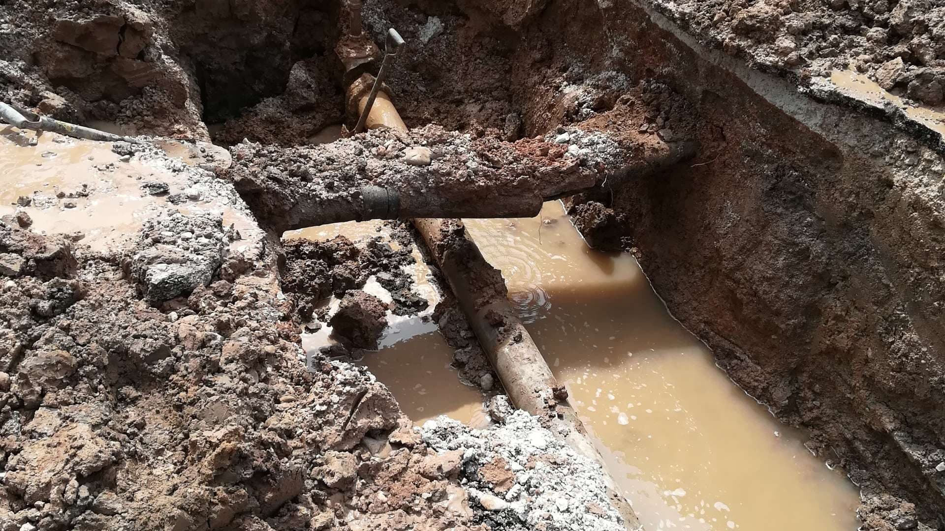 Tubería de agua enterrada con fuga y la zanja inundada